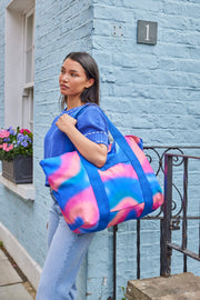 Woman holding a colorful tote bag in front of a blue brick building